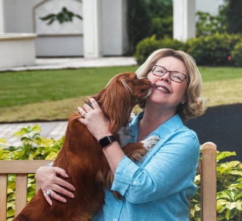 Linda Leatherbury smiles while holding a brown dog on an outdoor bench.