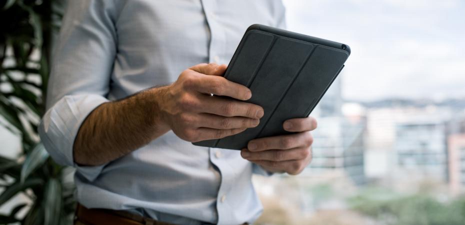 Image of man standing in front of window holding tablet in black base