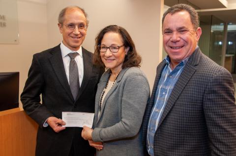 Dr. Gerson, Patti Berns, and Jonathon Berns stand smiling in the Case Comprehensive Cancer Center office. Dr. Gerson and Patti are holding a check.