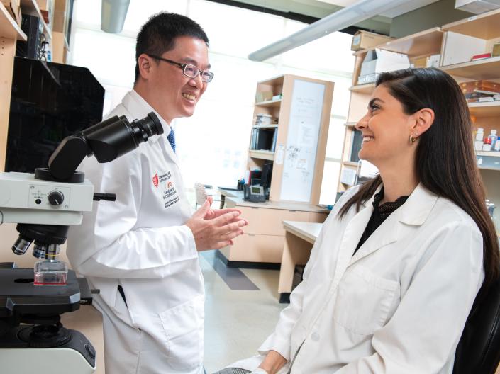 A mentor and mentee talking in the lab near a microscope