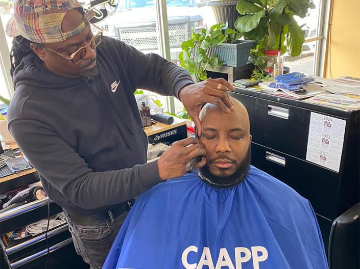 A barber tends to a client sitting in a chair