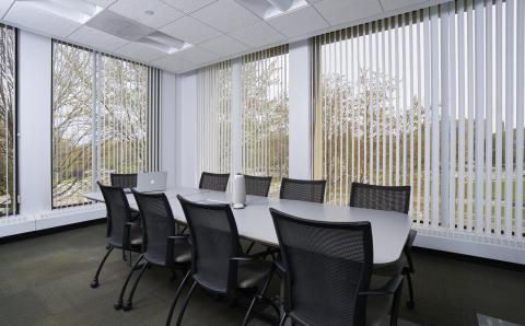 A large meeting table in the middle of an office surrounded by windows.