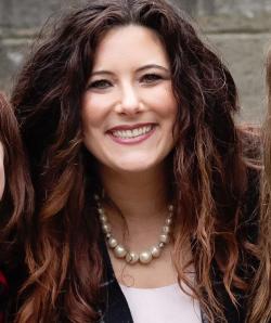 headshot of a woman with wavy hair, a pearl necklace, and a checkered blazer