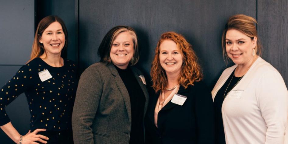 four women standing together in a line, facing the camera and smiling