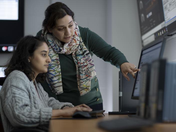 Image with instructor helping a student at a computer station 