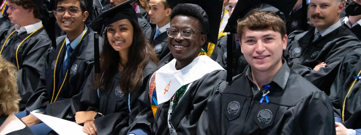 students sitting smiling in cap and gowns