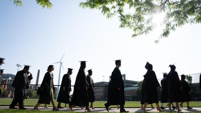 Students walking in cap and gown in grassy field