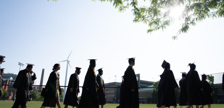 Students walking in cap and gown in grassy field