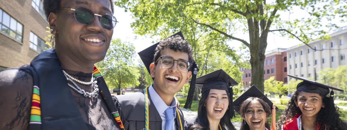 A group of five students smiling in their graduation regalia 