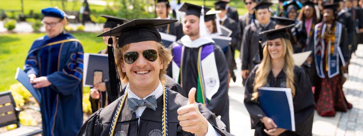 Photo of a graduating student in cap and gown giving a thumbs up