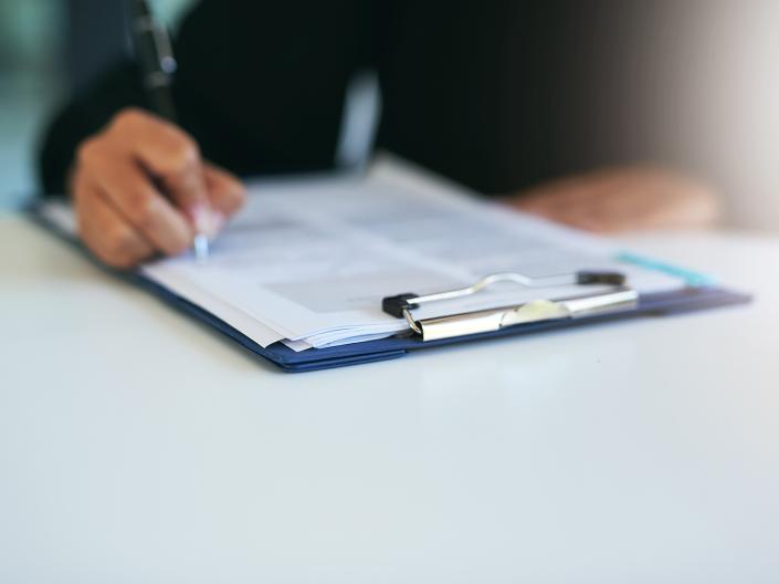 Close up of the hand of a business person focused on writing notes on a document while seated at a desk in a professional setting