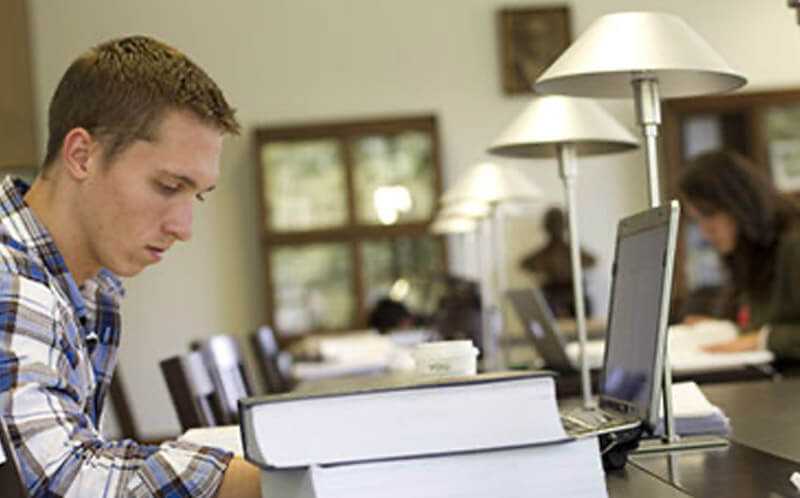 Photo of a Case Western Reserve University student working on a laptop, surrounded by large textbooks