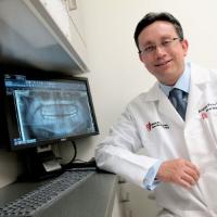 Dr. Pinto next to a computer with a dental x-ray on the screen