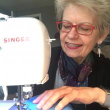 A smiling Dr. Jasinevicius uses a sewing machine to sew a mask.