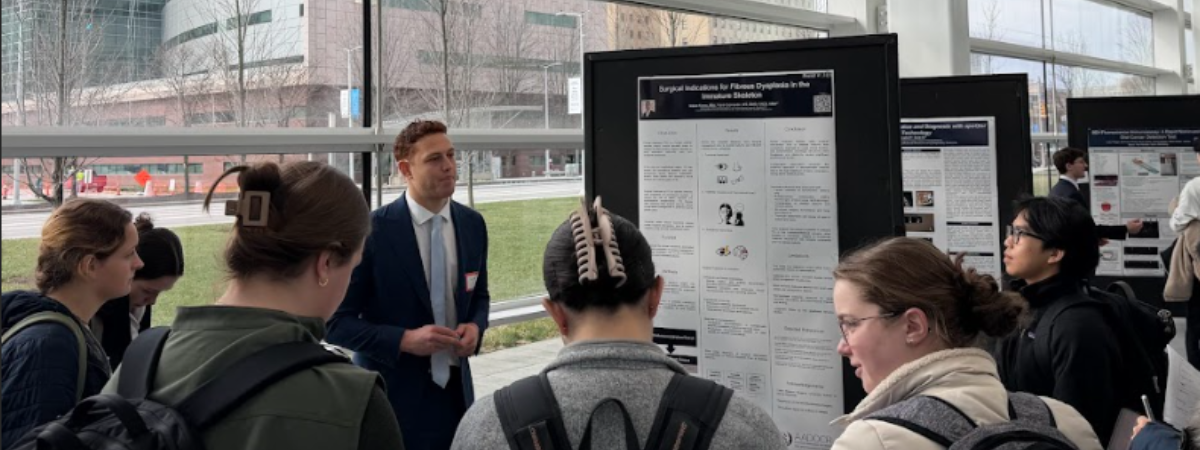 Students gather for a poster presentation at Professionals Day in front of a poster and glass wall.