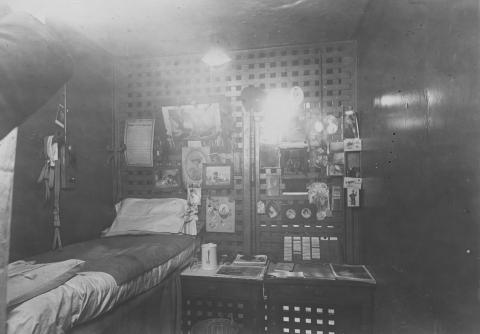 A black and white photo of a cell in the fourth Cuyahoga County Jail in 1910, with a cot on the left and photos hanging on the wall above
