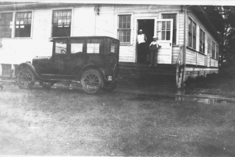 An old 1920s auto stands in front of a white frame building that house the Springvale Dance Hall.  A man and a boy stand on the steps leading into the building