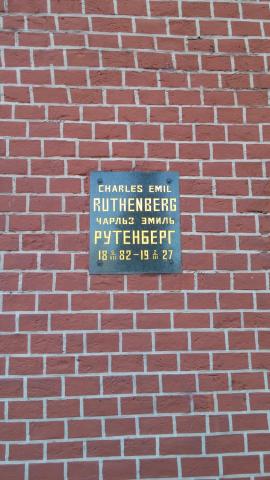 A small metal plaque with writing in English and Russian on a red brick wall marks the interment site of Charles Ruthenberg