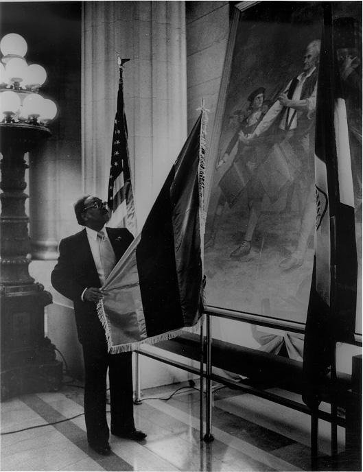 Mason A. Hargrave, Pres. of the Marcus Garvey Foundation, places the African national flag in the City Hall Rotunda to commemorate the Universal Negro Improvement Association, 10 Feb. 1984. CPL.