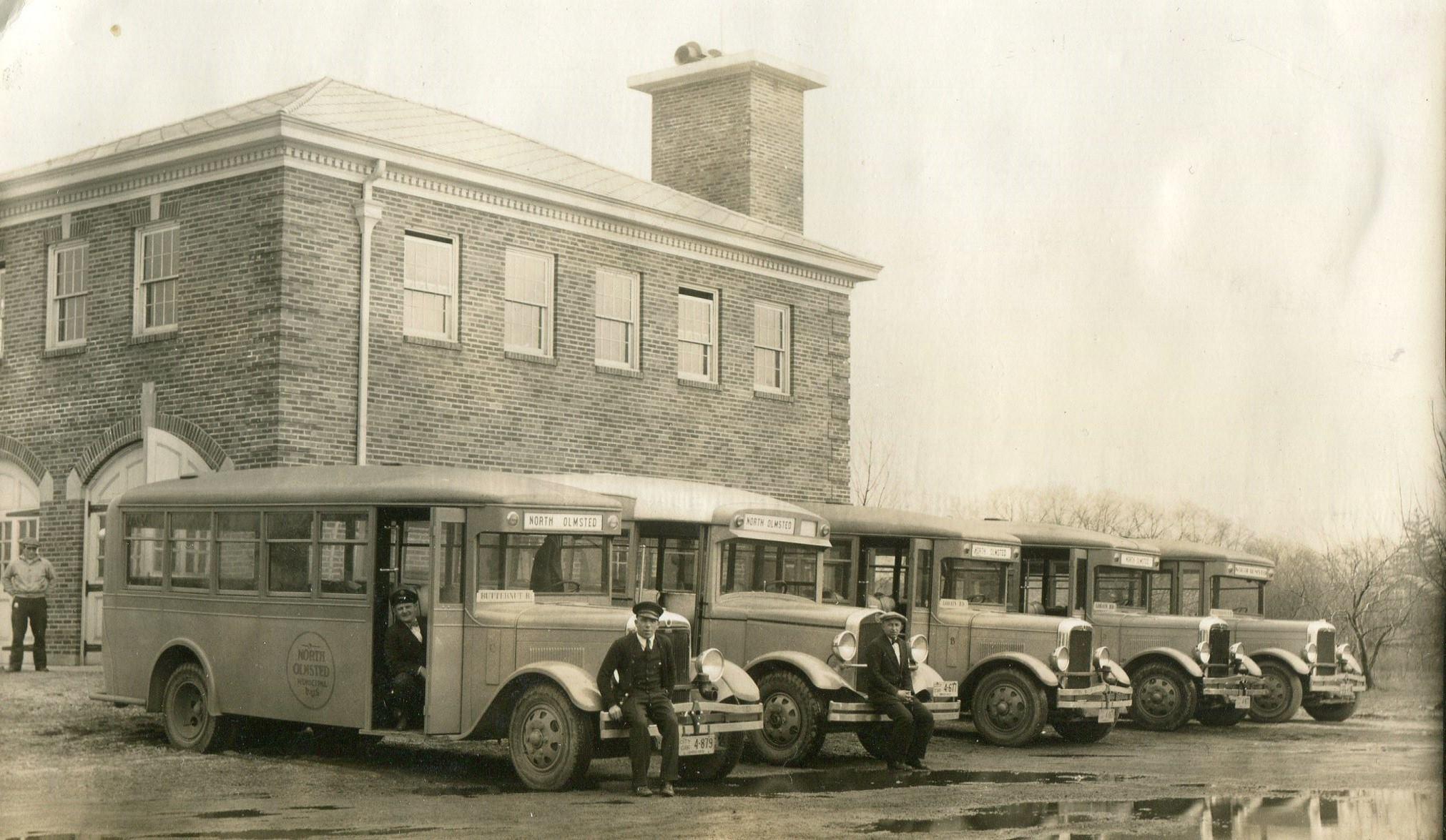 Five buses are lined up in a row in front of the North Olmsted Municipal Bus Line garage in this circa 1932 photograph with several drivers posed with the buses.