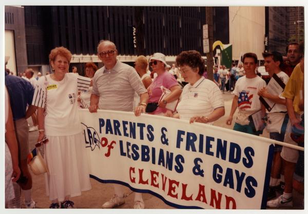 A color photo of members of the organization PFLAG Cleveland, including Jane and Robert Daroff, holding a banner for the organization at Cleveland Pride in 1991