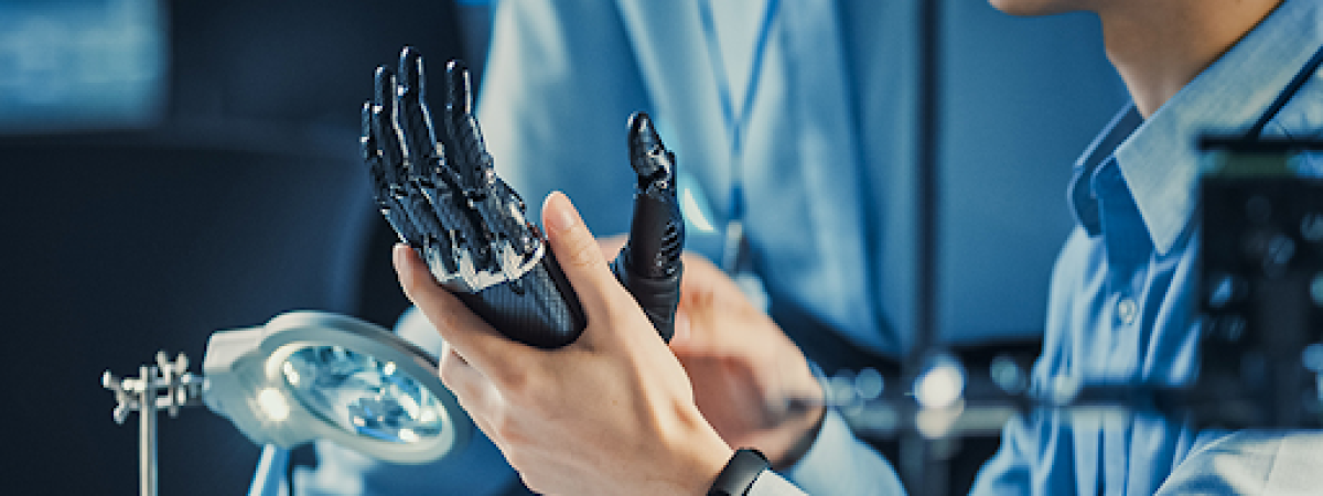 A close-up of a person's hands examining a robotic or prosthetic hand in a lab.