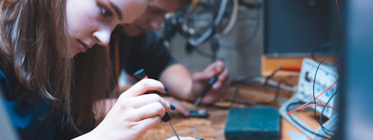 A focused female student works on a small electronic component with a screwdriver