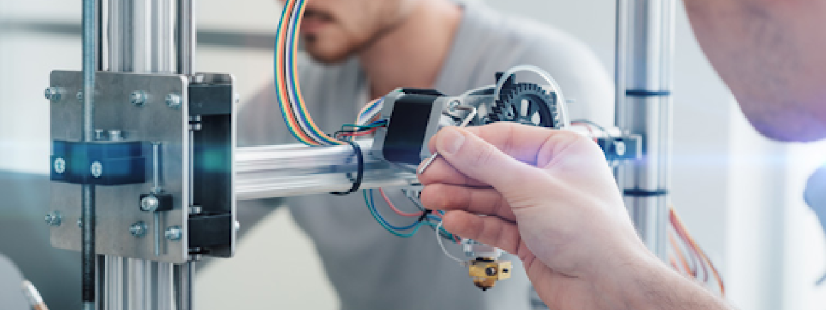A student is working on some technical equipment, while another student is visible in the background.