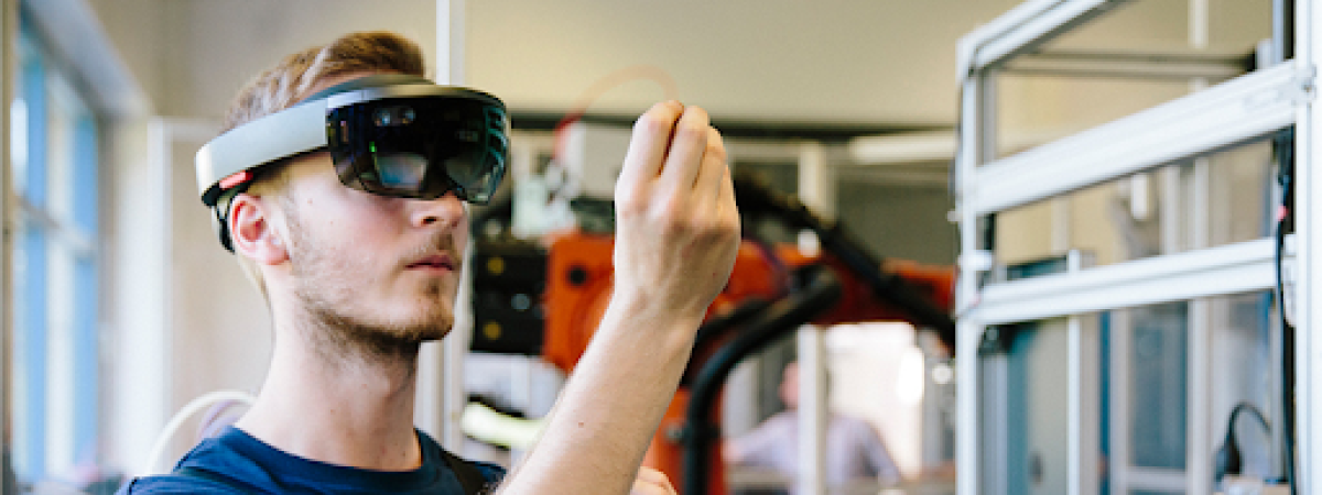 A man wearing a mixed reality headset examines an object in a lab.
