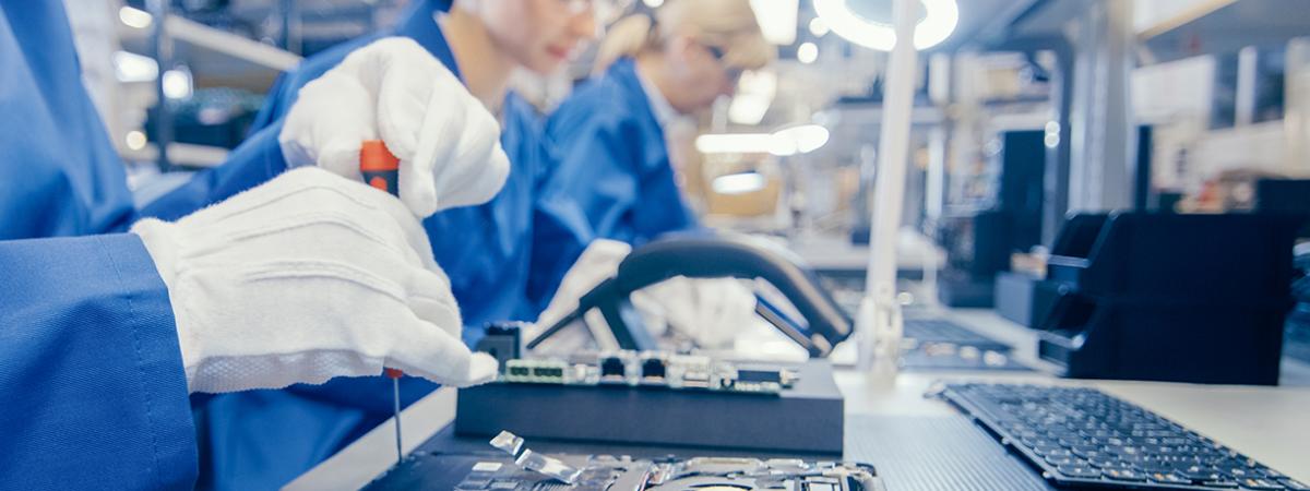 Engineers in a lab assembling electronics, with a screwdriver focused on a laptop in the foreground.