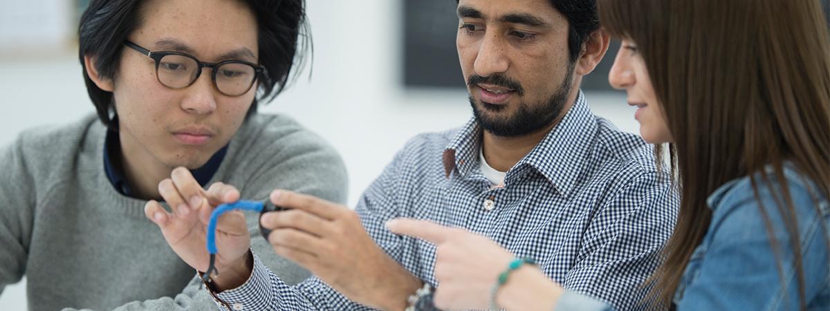 Three graduate engineering students collaborating and examining a technical component.