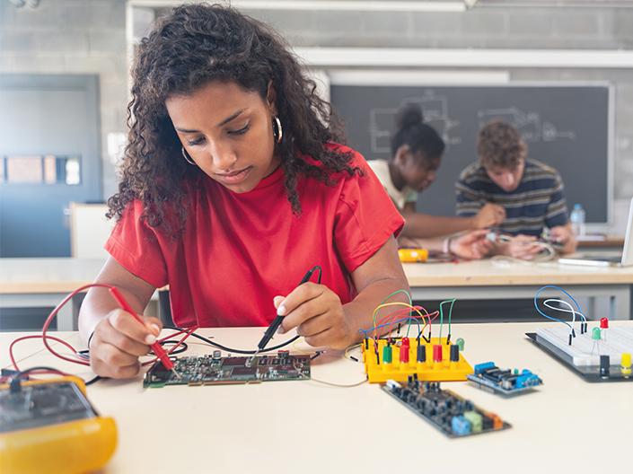 A focused female student testing a circuit board in a classroom setting