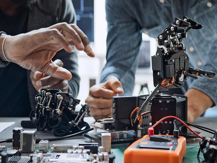 A close-up of two people's hands working on a robotic arm and other electronic components.