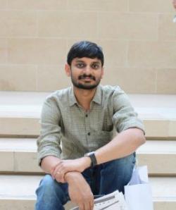 Photo of Sanmukh Kuppannagari sitting on stairs and holding onto blueprints.
