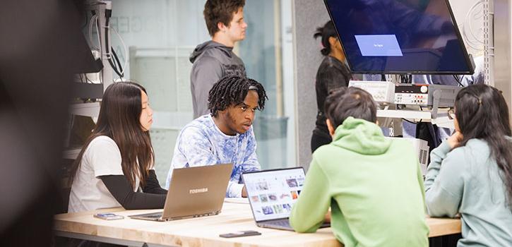 Students around a table with computers talking