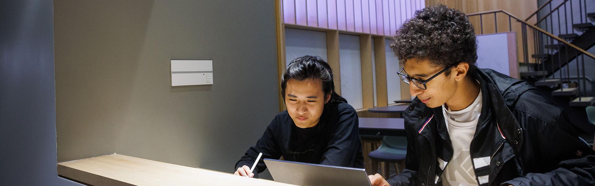 two students in a hallway looking at a computer
