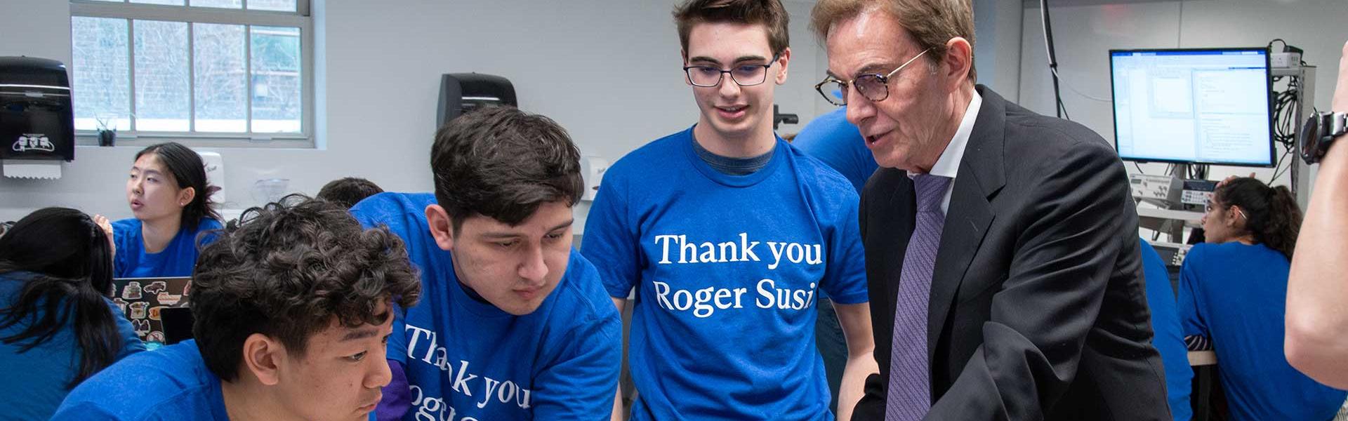 three students standing with an alum looking at a computer