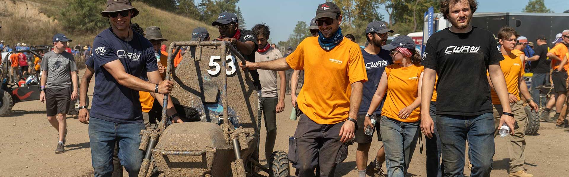 students walking with baja car covered in mud