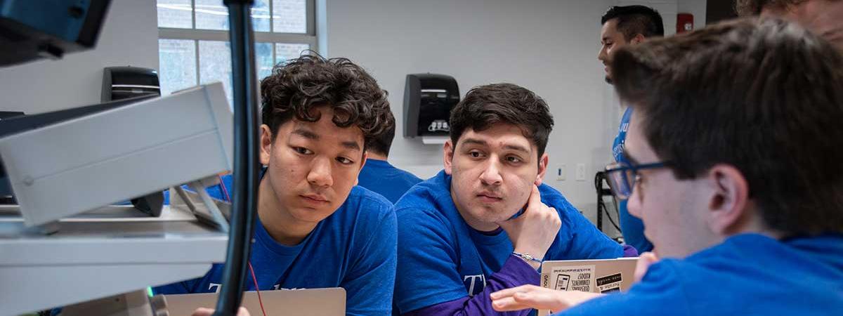 students sitting and looking at computer equipment