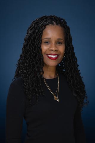 Headshot for Dr. Tiffani Monford. She is wearing all black and is smiling against a blue backdrop. 