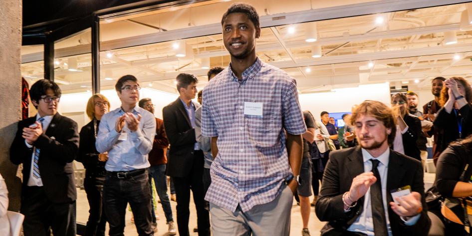 A man walking up to receive his prize at a competition while others applaud