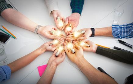 Artistic photo of nine people stretching their arms toward each other with a lightbulb in each hand