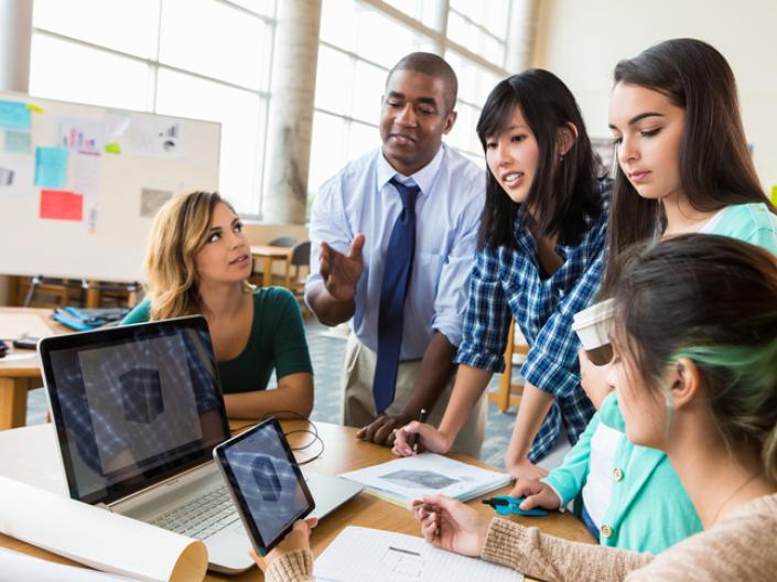 group of students standing around computer working together.