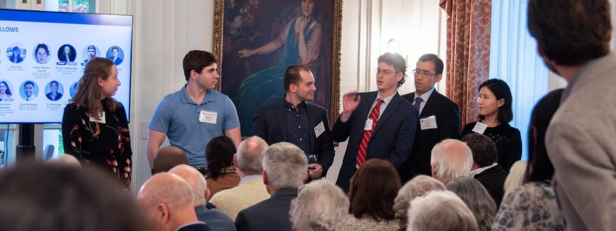 A diverse group of individuals in a room, focused on a screen that showcases a collection of pictures.
