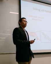 A man in a suit standing in front of a large screen displaying information.