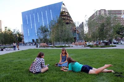 Three Case Western Reserve University students laying on the grassy area in Toby's Plaza in Uptown Cleveland with MOCA Cleveland in the background