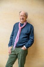 Billy Collins, in his late 70s, standing with a scarf against a tan background