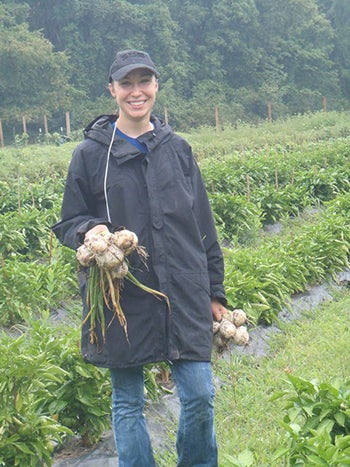 Student in large garden harvesting root plants, with large green trees in background