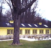 Outside view of Ceramic Studio at CWRU Farm, in yellow with dark roof and picnic tables and tree in foreground