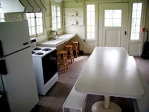 View of CWRU Pink Pig cottage kitchen, with white walls, tables and appliances